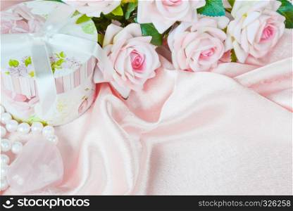 Pink roses, round gift box and a pearl necklace on a silk fabric, holiday pink composition with copy-space