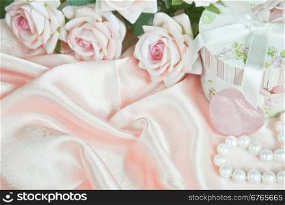 Pink roses, round gift box and a pearl necklace on a silk fabric