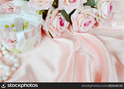pink roses, round gift box and a pearl necklace on a silk fabric