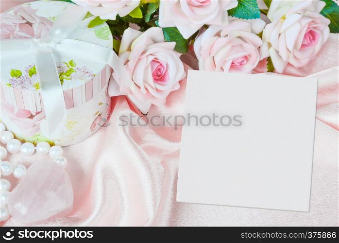 Pink roses, round gift box, white square blank paper sheet or canvas and a pearl necklace on a silk fabric, holiday pink composition with copy-space