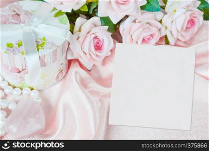 Pink roses, round gift box, white square blank paper sheet or canvas and a pearl necklace on a silk fabric, holiday pink composition with copy-space