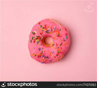 pink round donut with colored sprinkles on a pink background, top view