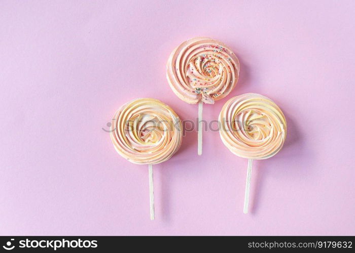 Pink round sweet meringues on a stick with decor lie on a pink background. Pink round sweet meringues on a stick lie on a pink background