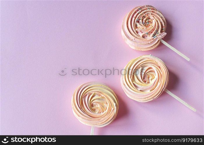 Pink round sweet meringues on a stick with decor lie on a pink background. Pink round sweet meringues lie on a pink background