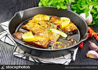 Pink salmon with a sauce of honey, lemon juice, garlic, hot pepper and soy sauce, lemon slices and a sprig of thyme in a frying pan on a towel, parsley on dark wooden background