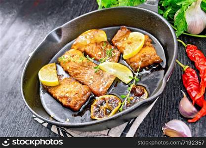 Pink salmon with a sauce of honey, lemon juice, garlic, hot pepper and soy sauce, lemon slices and a sprig of thyme in a frying pan on towel, parsley on wooden board background