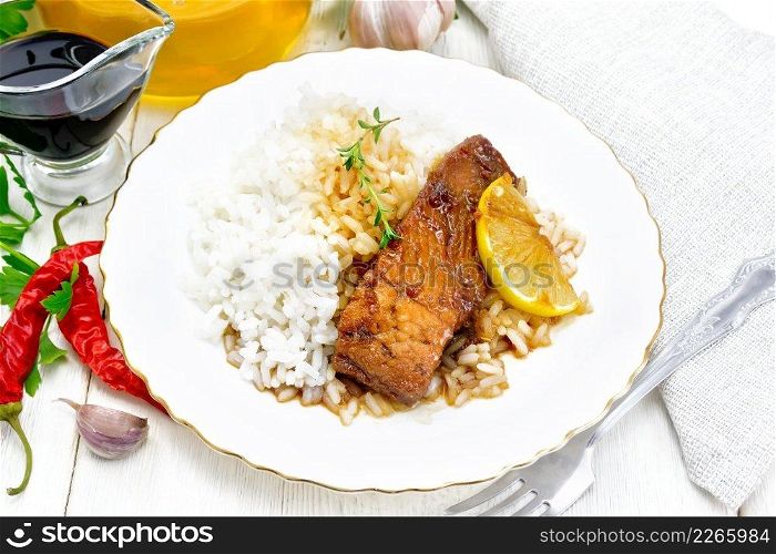 Pink salmon with honey, lemon juice and soy sauce, boiled rice, a slice of lemon and sprig of thyme in a plate, hot pepper, garlic, parsley, napkin and fork on white wooden background
