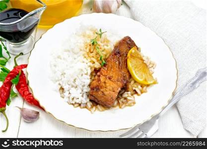 Pink salmon with honey, lemon juice and soy sauce, boiled rice, a slice of lemon and sprig of thyme in a plate, hot pepper, garlic, parsley, napkin and fork on white wooden background
