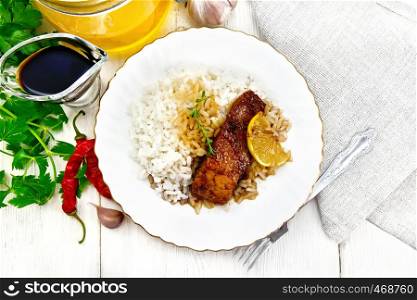 Pink salmon with honey, lemon juice and soy sauce, boiled rice, slice of lemon and sprig of thyme in a plate, hot pepper, garlic, parsley, napkin and fork on wooden board background