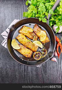 Pink salmon with honey, lemon juice, garlic, hot pepper and soy sauce, lemon slices and a sprig of thyme in frying pan on a napkin, parsley on black wooden background from above