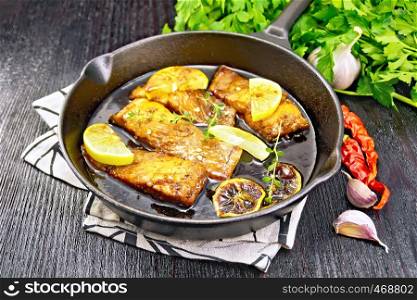 Pink salmon with honey, lemon juice, garlic, hot pepper and soy sauce, lemon slices and a sprig of thyme in frying pan on a napkin, parsley on black wooden background