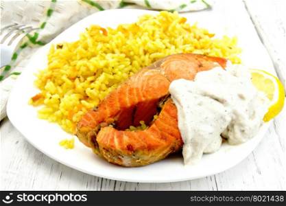 Pink salmon with lemon, milk sauce and rice with turmeric in a dish, a towel and a fork on the background of wooden boards
