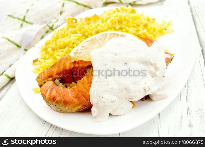 Pink salmon with lemon, milk sauce and rice with turmeric in a dish, kitchen towel on a background of wooden boards