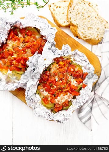 Pink salmon with zucchini, tomatoes, onions, garlic and thyme, baked in foil, fork and bread on wooden board background from above