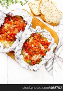 Pink salmon with zucchini, tomatoes, onions, garlic and thyme, baked in foil, fork and bread on wooden board background from above