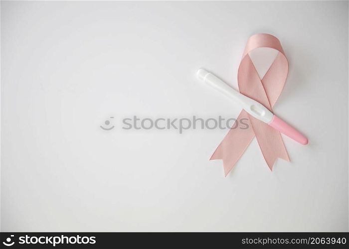 Pink satin breast cancer awareness ribbon with blank pregnancy test isolated on white background top view space for text. Pink satin breast cancer awareness ribbon with blank pregnancy test isolated on white background top view