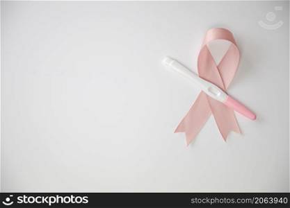 Pink satin breast cancer awareness ribbon with blank pregnancy test isolated on white background top view space for text. Pink satin breast cancer awareness ribbon with blank pregnancy test isolated on white background top view