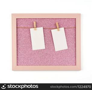 pink shiny frame with ropes and empty white paper sheets hanging on wooden clothespins, place for photo and inscription