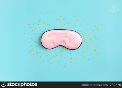 Pink silk sleep mask for eyes and gold stars confetti on a blue background. Top view Flat lay Copy space. Concept eye protection from light for good sleep and melatonin production.. Pink silk sleep mask for eyes and gold stars confetti on a blue background. Top view Flat lay Copy space. Concept eye protection from light for good sleep and melatonin production