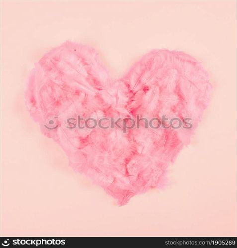 pink soft feather heart shape peach colored background. Beautiful photo. pink soft feather heart shape peach colored background