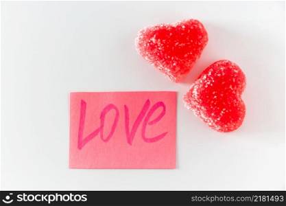 Pink sticker with the word love and two red marmalade in the shape of a heart. Symbol of love on a white background. Sticker with the word love and marmalade