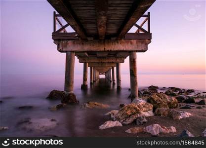 Pink sunset as seen from below an old wooden jetty on a beach in the Costa del Sol in Marbella, Spain. Long exposure.
