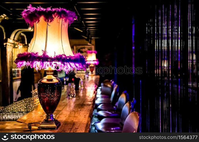 Pink table lamp on old school traditional wooden bar counter in a dark room