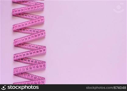 Pink tape measure spirally laid on pink background. Copy space Top view. Pink tape measure spirally laid on pink background.