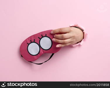 pink textile sleep mask in a female hand sticking out of a bull in a pink paper background, insomnia