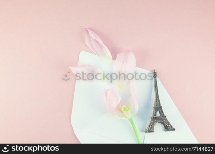 Pink tulip with petals in opened paper envelope letter with eiffel tower miniature on a pink background. Flat lay top view. Romantic love memories concept