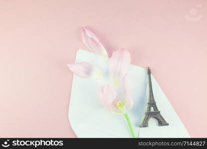 Pink tulip with petals in opened paper envelope letter with eiffel tower miniature on a pink background. Flat lay top view. Romantic love memories concept