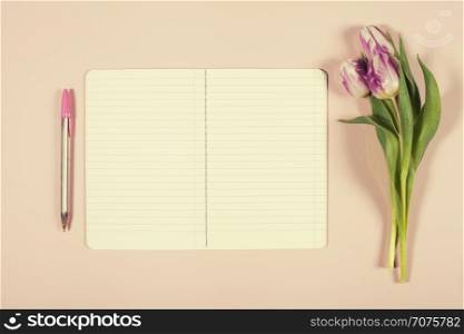 Pink tulips and notebook on pink background. Flat lay. Overhead view.