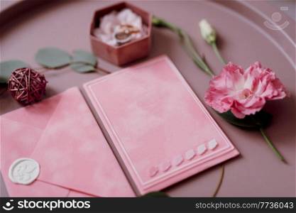 pink wedding invitation in a gray envelope on a table with green sprigs