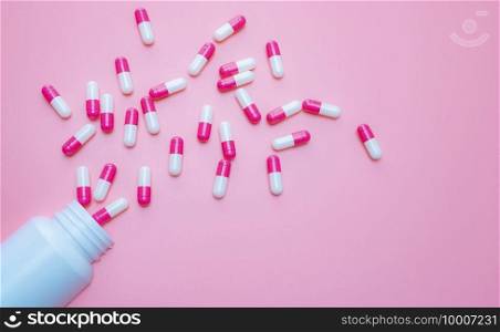 Pink-white capsules pill spilled out from plastic bottle container on pink background. Antibiotics drug resistance. Antimicrobial capsule pills. Pharmaceutical industry. Pill for happy love concept.