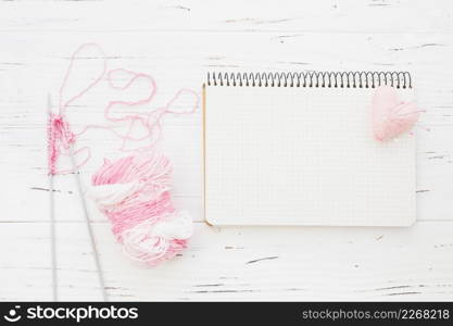 pink yarn with crochet beside notepad heart wooden background