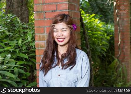 Pinoy woman in a green garden on farm, leaning against brick pillar