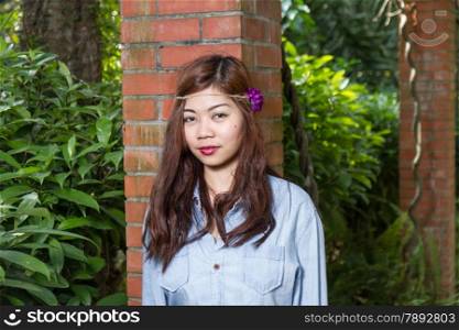 Pinoy woman in a green garden on farm, leaning against brick pillar