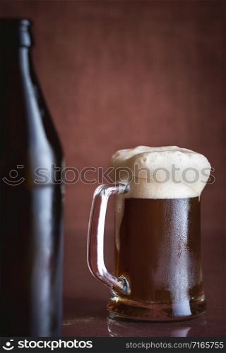 Pint of black beer with foam and frost, on brown background. Cold glass of beer. Summer drink. Dark beer in a glass mug. Alcohol beverage. Fresh beer.