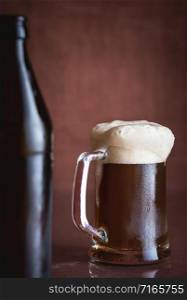Pint of black beer with foam and frost, on brown background. Cold glass of beer. Summer drink. Dark beer in a glass mug. Alcohol beverage. Fresh beer.