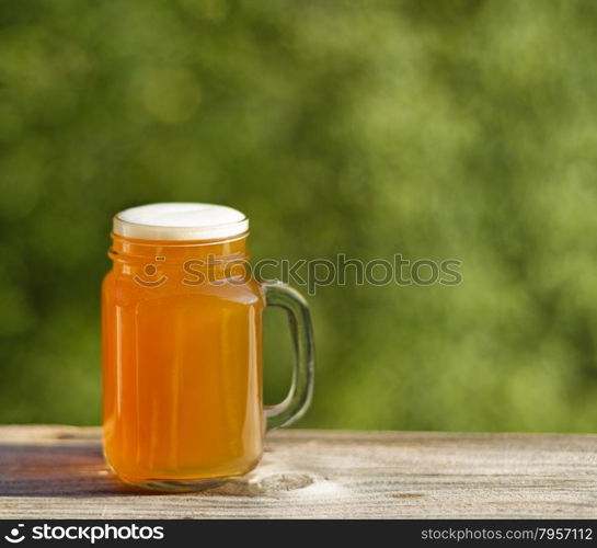Pint of golden beer on rustic wood with blurred out green trees in background. Freshly poured to enjoy the outdoors.