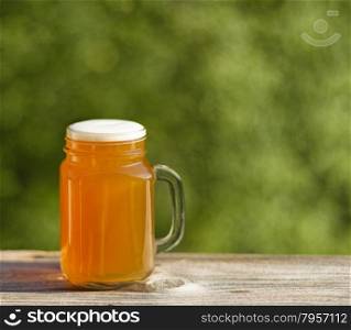 Pint of golden beer on rustic wood with blurred out green trees in background. Freshly poured to enjoy the outdoors.