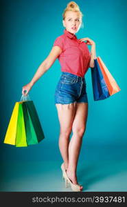 Pinup blond girl young woman in retro style buying clothes. Client customer holding colorful paper shopping bags on vibrant blue. Retail and sale. Studio shot.