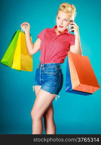 Pinup blond girl young woman in retro style calling on the mobile phone. Client customer holding colorful paper shopping bags on vibrant blue. Retail and sale. Studio shot.