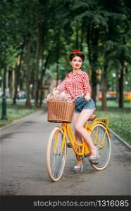 Pinup girl on retro bicycle with backet of flowers. Pin-up style pretty woman