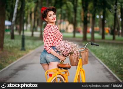 Pinup girl on retro bicycle with backet of flowers. Pin-up style pretty woman. Pinup girl on retro bicycle with backet of flowers