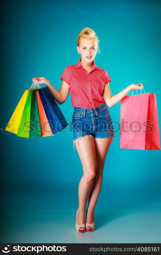 Pinup girl young woman in retro style buying clothes. Client holding colorful shopping bags on vibrant blue. Retail and sale. Studio shot.