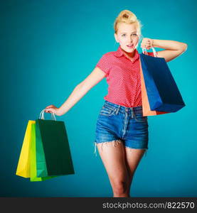 Pinup girl young woman in retro style buying clothes. Client holding colorful shopping bags on vibrant blue. Retail and sale. Studio shot.