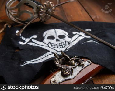 pirate flag jolly roger sword and pistol lying on a dark wooden surface. sword flag pistol