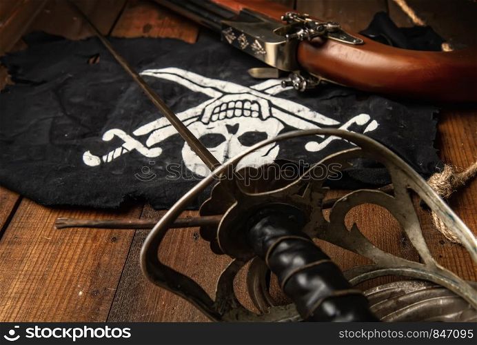 pirate flag jolly roger sword and pistol lying on a dark wooden surface. sword flag pistol