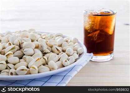 Pistachio nuts in a bowl and drink is placed on a wooden floor.